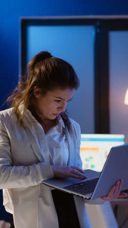 Focused manager woman checking business reports standing in start up office late at night holding...