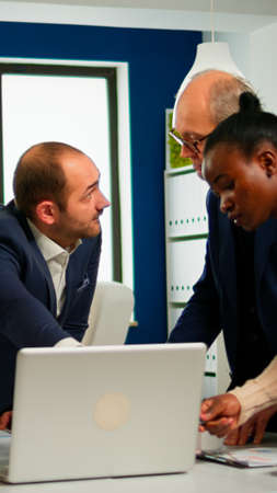Diverse businesspeople working in teamwork discussing project strategy using laptop standing at...