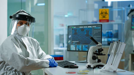Portrait of tired scientist in coverall looking at camera sitting in modern equipped laboratory....