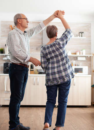 Joyful old man and woman dancing in kitchen early in the morning, relaxing after having healthy breakfast. Happy senior couple having fun, retired persons in cozy home enjoying lifeの写真素材