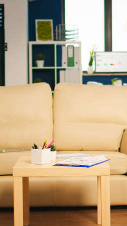 Modern business relax zone interior with confortable couch and orange chair. Rest area in business center with small sofa, shot of empty room with modern furniture, white shelves and blue wall.の写真素材
