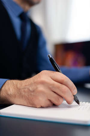 Close up of man taking notes on notebook while working from home. Elderly man entrepreneur in home...