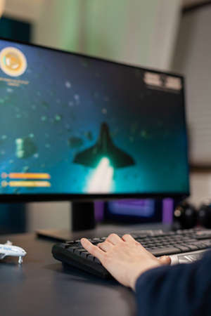 Closeup of Hand of player on professional keyboard with RGB during space shooter tournament. Pro gamer playing on gaming desk in home studio streaming online videogamesの写真素材