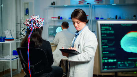 Back view of woman patient wearing performant brainwave scanning headset sitting in medical...