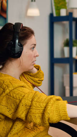 Focused woman gamer sitting on desk, putting on headset with a mic and starts playing video game....