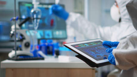 Back view of scientist in coverall analyzing virus evolution looking on digital tablet. Team of...