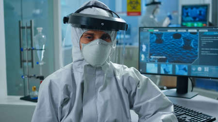 Overworked woman chemist sitting in modern equipped lab wearing coverall looking tired at camera....