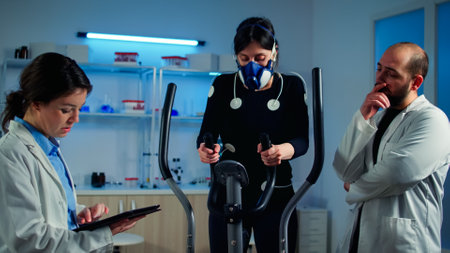 Woman athlete with mask doing fitness exercises in science sport lab with electrodes attached while...
