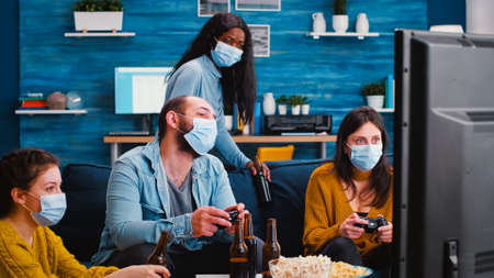 Sad multiethnic group of friends after lose at gaming competiton with face covers with mask during...