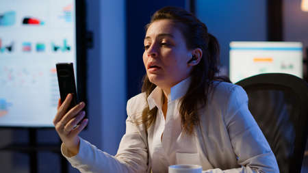 Entrepreneur having virtual meeting using smartphone with wireless headphone sitting at desk in...