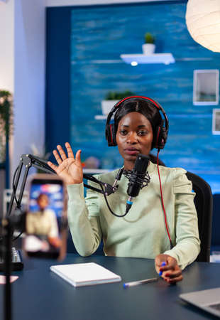 African blogger looking at camera and waving to camera recording episode for online show. Speaking...