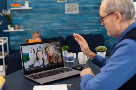 Senior man waving at daughter and niece during video conference. Happy grandfather saying hello in...