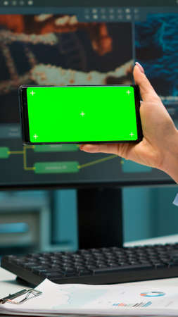 Close up of scientist woman holding smartphone with green mockup in modern equipped lab. Team of...