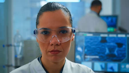 Close up of tired scientist doctor looking at camera smiling working in equipped lab. Chemist...