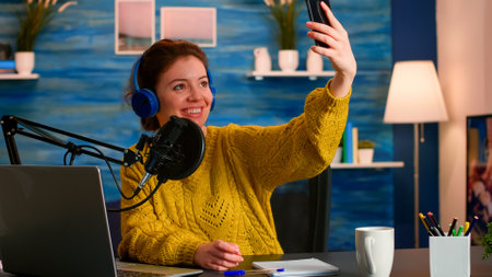 Social media influencer using phone for taking selfie recording podcast series for audience. On-air online production internet broadcast show host streaming live content for digital video vlogの写真素材