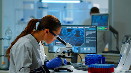Scientist looking at biological samples under microscope typing on pc. Team of chemists working in...