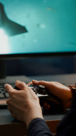 Closeup of competitive woman player holding joystick playing space shooter video games at powerful computer late night. Professional gamer using wireless controller for online gaming championshipの写真素材