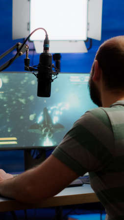 Streamer cyber performing space shooter video game on RGB powerful computer talking with players on stream chat and microphone during professional competition. Player man streaming in home studioの写真素材