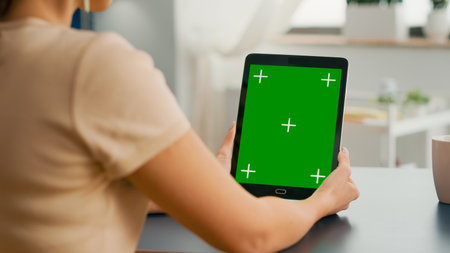 Freelancer woman holding tablet computer with mock up green screen chroma key display sitting on office room. Caucasian female browsing on internet for online project using isolated deviceの写真素材