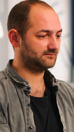 Close up of authentic manager sitting at table in modern startup business office sending mails typing on laptop smiling and greeting colleague. Man working in financial company with diverse team.の写真素材