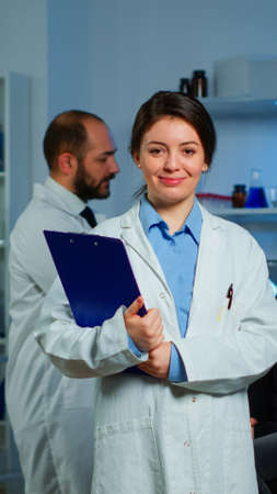 Portrait of scientist neurologist researcher looking at camera smiling while coworker discussing with patient in background about brain functions, nervous system, tomography scan working in laboratoryの写真素材
