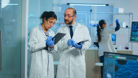 Group of medical researchers discussing about vaccine development standing in equipped lab pointing...