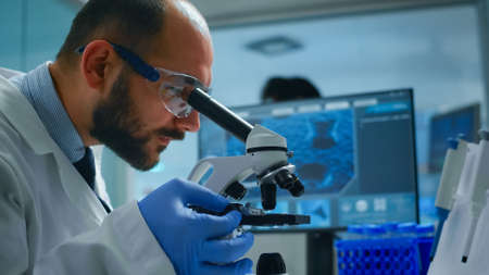 Lab technician examining samples and liquid using microscope in equipped laboratory. Scientist...
