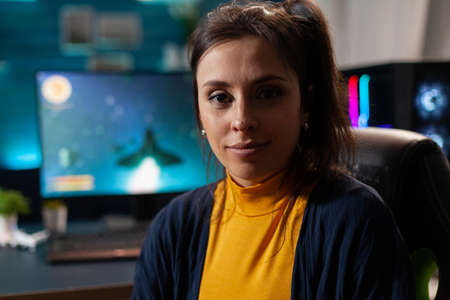 Portrait of woman gamer looking into camera after playing space shooter games using professional RGB keypad on powerful computer. Caucasian pro player streaming online videogames in home studioの写真素材