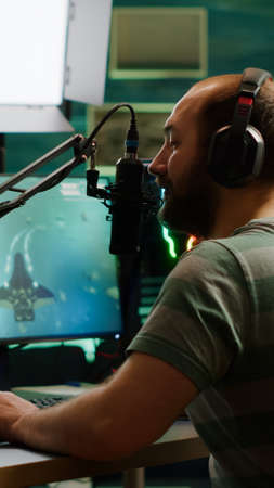 Pro cyber man streaming videogame, reading on stream chat and playing space shooter on RGB powerful computer. Streamer sitting on gaming chair playing game during online esports tournament.の写真素材
