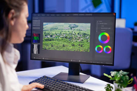 Focused editor retoucher editing color grade on professional computer sitting at desk in creative office at midnight. Freelancer video editor start up new movie project processing audio film montage.の写真素材