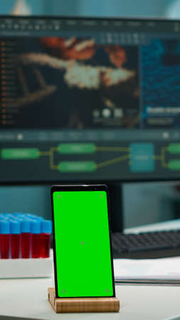Display phone with green screen, mock up on template placed on desk in scientific lab while team of medical researcher scientists analysing virus evolution at digital monitor conducting experimentの写真素材