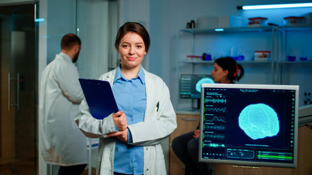 Portrait of medical neurologist researcher looking at camera smiling holding clipdoard while coworker discussing with patient about brain health care, nervous system, tomography scan working in labの写真素材