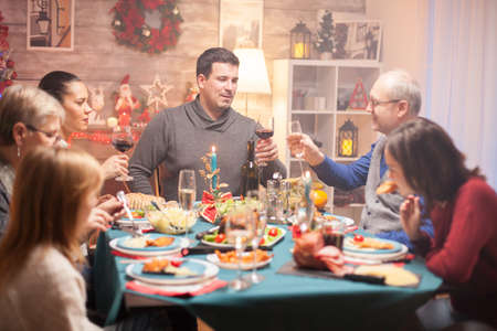 Happy senior man and his son clinking a glass of wine at christmas family dinner.の写真素材
