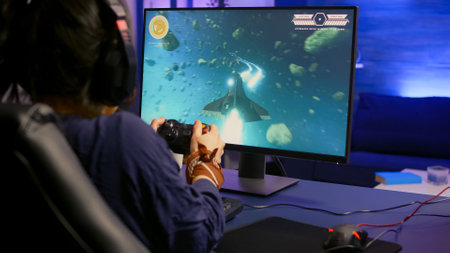 Back view of pro gamer winning space shooter game using headphones. Player using joystick for online...