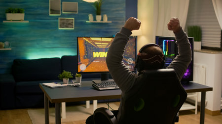 Videogamer player raising hands after winning first person shooter competition wearing hradphones. Professional pro gamer playing online video games with new graphics on powerful computerの写真素材