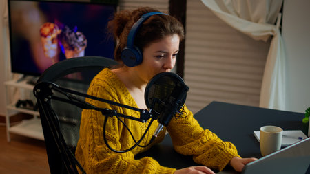 Blogger speaking at microphone with followers livestreaming typing on laptop. Online show On-air production internet broadcast host streaming live content, recording digital social media communicationの写真素材