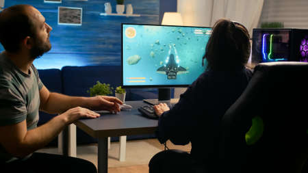 Pro gamer couple playing space shooter games sitting on gaming chiar wearing headphones. Professional digital player streaming video game with modern graphics for online game championshipの写真素材