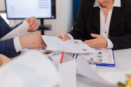 Close up view desk full of papers stats shown on charts and diverse businesspeople. Colleagues...