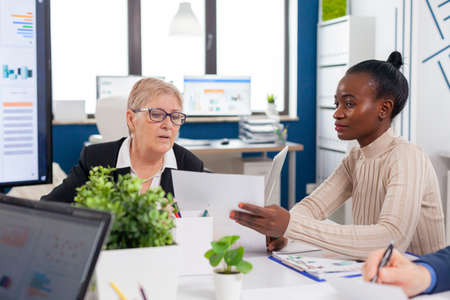 African employee in financial business board meeting room talking with senior entrepreneur investors looking analysing project documents. Personal colleagues of startup.の写真素材