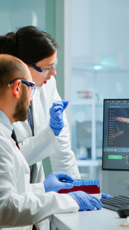 Team medical scientist conducting DNA experiments looking in computer holding test tube with blood sample working in science laboratory. Lab engineers in white coat analysing vaccine developmentの写真素材