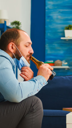 Group of friends with protection masks playing chess while drinking beer, clinking bottles recreating in living room during new normal party.の写真素材
