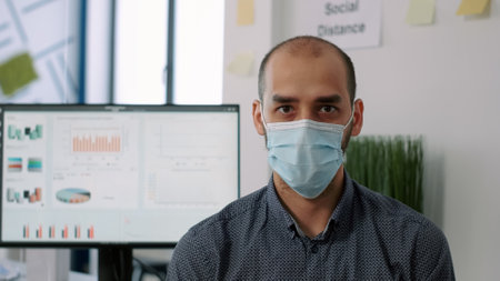 Closeup of employee wearing protection medical face mask looking into camera while standing on chiar...
