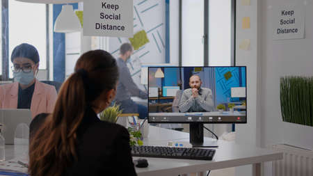 Back view of business woman with face mask disscusing on videocall conference with remotely coworkers. Executive freelancer working in new normal company office during  pandemicの写真素材