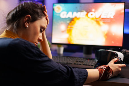 Pro videogames keeping his head on hand after losing space shooter game using wireless joystick . Defeated gamer wearing vr headphone for online championship sitting on gaming chair late at nightの写真素材