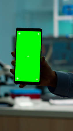 Close up of chemists hand holding smartphone with green screen standing in biological laboratory while nurse bringing blood samples. Scientist using smartphone with mockup, chroma key displayの写真素材