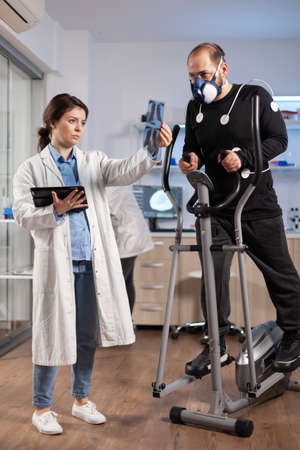 Team of doctor researchers monitoring endurance of man performance sports wearing mask running cross...