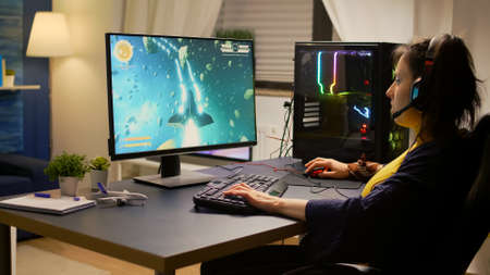 Gamer playing online space shooter video games using powerful computer and RGB keyboard. Player wearing headphones and talking into microphone with other players for winning online tournamentの写真素材