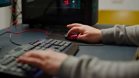 Close up hands shot of man player typing on RGB keyboard buttons while playing online shooter video...