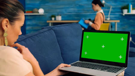 Business woman searching lifestyle advertising using isolated pc lying on sofa in living room. Caucasian female working with laptop computer with mock up green screen chroma keyの写真素材