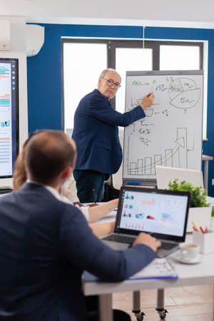 Confident man business coach giving flipchart presentation training diverse workers group at workshop, Serious speaker boss executive, business trainer explaining development strategy to motivated mixed race employees.の写真素材